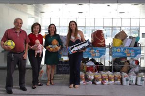 Foto mostrando, lado a lado, servidores do TRT-18 e representantes da entidade beneficente que recebeu as doações. Cada um está segurando um brinquedo que foi doado. Ao fundo, carrinhos com os itens arrecadados.