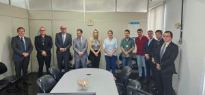 Foto colorida do corregedor com a equipe da 3ª VT de Anápolis. Tratam-se de onze pessoas, sendo nove homens e duas mulheres. Eles estão de pé, atrás de uma mesa e posando para foto.