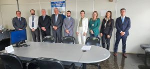 Foto colorida do corregedor com a equipe da 4ª VT de Anápolis. Tratam-se de nove pessoas, sendo seis homens e três mulheres. Eles estão de pé, atrás de uma mesa e posando para foto.