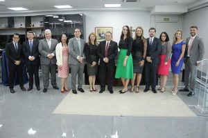 Foto colorida mostrando um grupo de pessoas de pé, lado a lado, posando para foto. Tratam-se de 13 pessoas, sendo seis mulheres e sete homens. Todos estão usando roupas formais.
