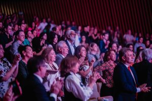 Foto do público da palestra. Estão todos sentados em cadeiras que preenchem o auditório.