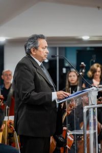 Foto colorida do presidente do TRT-18, desembargador Geraldo Nascimento. Trata-se de um homem branco, de cabelos grisalhos. Ele usa um terno preto e está de pé atrás de púlpito enquanto fala ao microfone de mesa.