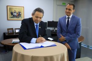 Foto mostrando o presidente do TRT em pé, assinando um acordo. Ao lado dele, observando o ato e também em pé, o procurador-geral do Estado de Goiás