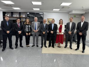 Várias pessoas em pé numa sala ampla posando para foto. Atrás, uma estante de vidro e madeira