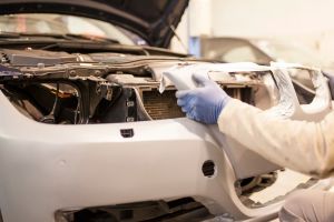 na imagem a mão de um trabalhador arrumando a parte de lataria de um veículo