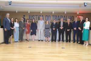A imagem mostra um grupo de pessoas posando em frente ao painel "Justiça do Trabalho". São 13 pessoas alinhadas, vestidas formalmente, sugerindo uma cerimônia oficial.