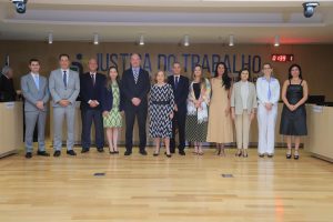 A imagem mostra um grupo de 11 pessoas em pé, alinhadas e vestidas formalmente, em um ambiente oficial com o painel "Justiça do Trabalho" ao fundo. A disposição e o cenário sugerem a captura de um momento solene.