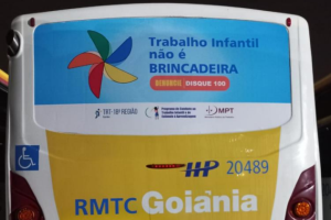 Banner em ônibus mostra imagem em fundo azul com um catavento colorido à direita e à esquerda a frase "Trabalho infantil não é BRINCADEIRA". DENUNCIE. DISQUE 100