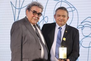 Dois homens de terno e gravata posam para foto, o da direita, desembargador Geraldo Nascimento, segura o troféu.