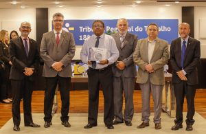 Vários homens em pé. O do meio segura um troféu