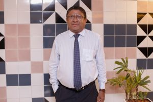 Um homem em pé, com a mão no bolso, vestindo camisa social e gravata