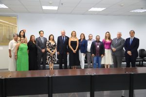 A imagem mostra um grupo de pessoas formalmente vestidas, posando juntas em uma sala com mesas ao fundo, sugerindo um evento institucional ou uma reunião oficial.