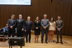 Grupo de sete pessoas em trajes formais, entre eles, cinco homens e duas mulheres, posando para uma foto.