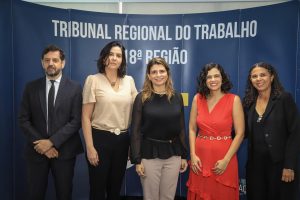grupo de cinco pessoas vestindo trajes formais com o símbolo do tribunal ao fundo