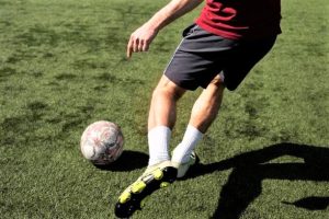 Um jogador de futebol de short preto e uniforme vermelho prestes a chutar uma bola