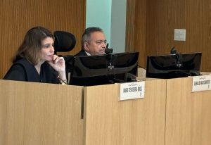 Duas pessoas sentadas numa bancada de frente para uma tela de computador.