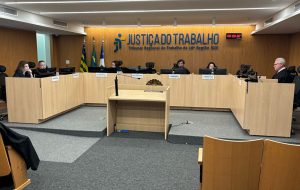 Sala de sessão da 1ª Turma. Pessoas com toga ao redor de uma bancada em U. No fundo, a logo da Justiça do Trabalho