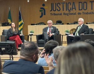 Uma mulher e dois homens sentados em poltronas no palco de um auditório.