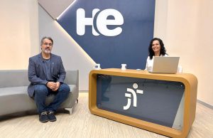 Um homem sentado em uma poltrona e uma mulher numa bancada. Eles olham para a câmara. Ao fundo, a logomarca do programa hora extra. Embaixo da bancada, a logomarca da Justiça do Trabalho
