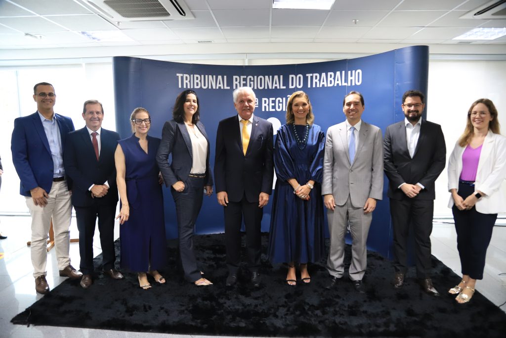 Várias pessoas em pé posando para foto. Ambiente fechado.