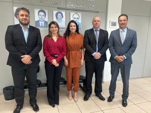 Pessoas posando lado a lado para foto. São três homens usando terno e duas mulheres usando roupas formais.
