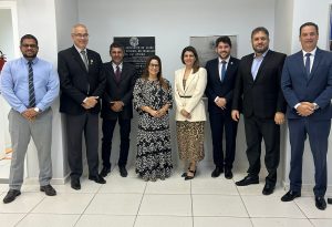 Oito adultos posam para uma foto em um ambiente interno com paredes claras e piso claro com faixas pretas. 