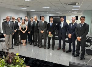 Onze pessoas, a maioria homens de terno, e uma mulher, reunidas em um escritório ou sala de conferências com aspecto formal.