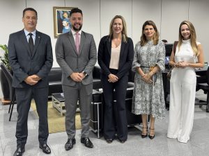 Pessoas posando para foto lado a lado. São dois homens usando terno e três mulheres usando roupas formais.