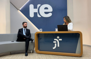 Foto da entrevista, que mostra a apresentadora à direita atrás de uma bancada e o entrevistado à esquerda, de terno, sentado em um sofá. Atrás, um painel com a logo do programa