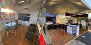 A imagem é uma colagem panorâmica mostrando diferentes perspectivas do interior e exterior de um estande de exposição.