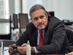 Homem de terno preto e gravata vermelha durante audiência de conciliação