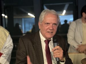 Homem usando terno escuro e gravata grená fala ao microfone