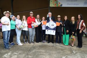 Um grupo de pessoas posa para uma foto, algumas segurando cestas de frutas e legumes e outras um cartaz.