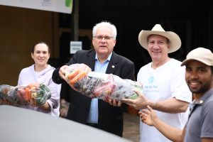 Três homens e uma mulher posam para uma foto, segurando sacolas cheias de vegetais.