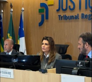 Três pessoas sentadas numa bancada com a logo da Justiça do Trabalho atrás