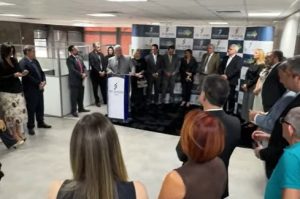Imagem mostra o coordenador do Cejusc, juiz Eduardo Thon, ao centro, durante seu discurso, e pessoas assistindo.