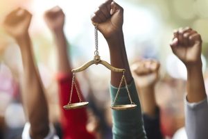 mãos em punho para cima e uma mão negra segurando a balança da Justiça
