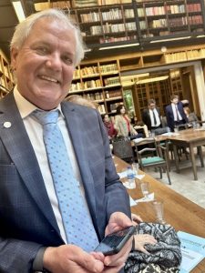 Desembargador Eugênio Cesário sentado em uma biblioteca. Ele sorri e posa para foto.