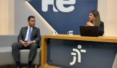 Um homem sentado em uma poltrona e uma mulher numa bancada. Eles olham para a câmara. Ao fundo, a logomarca do programa hora extra. Embaixo da bancada, a logomarca da Justiça do Trabalho