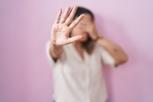Mulher em pé com as mãos sobre o rosto e a outra estendida em sinal de pare.