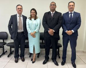 Quatro pessoas, sendo três homens e uma mulher, estão de pé e posando para a foto em um ambiente interno. Eles estão alinhados, com a mulher no centro.