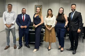 Uma fotografia de seis pessoas, três homens e três mulheres, em pé em um escritório. 