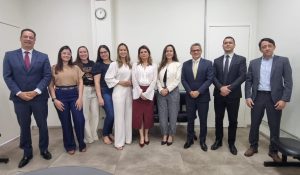 
Um grupo de aproximadamente dez advogados e advogadas está posando para uma foto em pé, em um escritório. A maioria das mulheres está no centro da imagem.