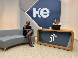 Uma mulher sentada em uma poltrona e um mulher numa bancada. Elas olham para a câmara. Ao fundo, a logomarca do programa hora extra. Embaixo da bancada, a logomarca da Justiça do Trabalho