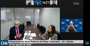 Print da transmissão ao vivo do evento mostra em destaque o desembargador Welington e a servidora Lara, ele um homem de cabelos grisalhos e terno, ela uma mulher de cabelos castanhos e casaco preto e branco, estão em volta de uma mesa; à direita, imagem do intérprete de Libras
