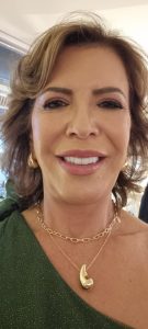 Uma mulher com cabelo curto, brincos de argola e um colar dourado está sorrindo e posando para uma foto de perto.