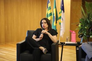 Mulher sentada em uma poltrona fala ao microfone