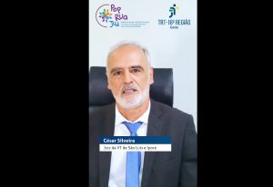 Homem usando terno escuro e gravata azul fala com o espectador