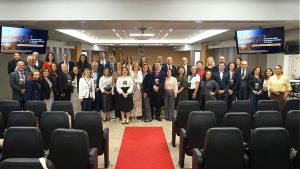 A imagem mostra várias pessoas em pé, lado a lado, posando para uma foto em um auditório