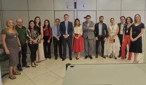 Um grupo grande de pessoas, homens e mulheres em trajes sociais ou casuais de negócios, posando em pé em um corredor.